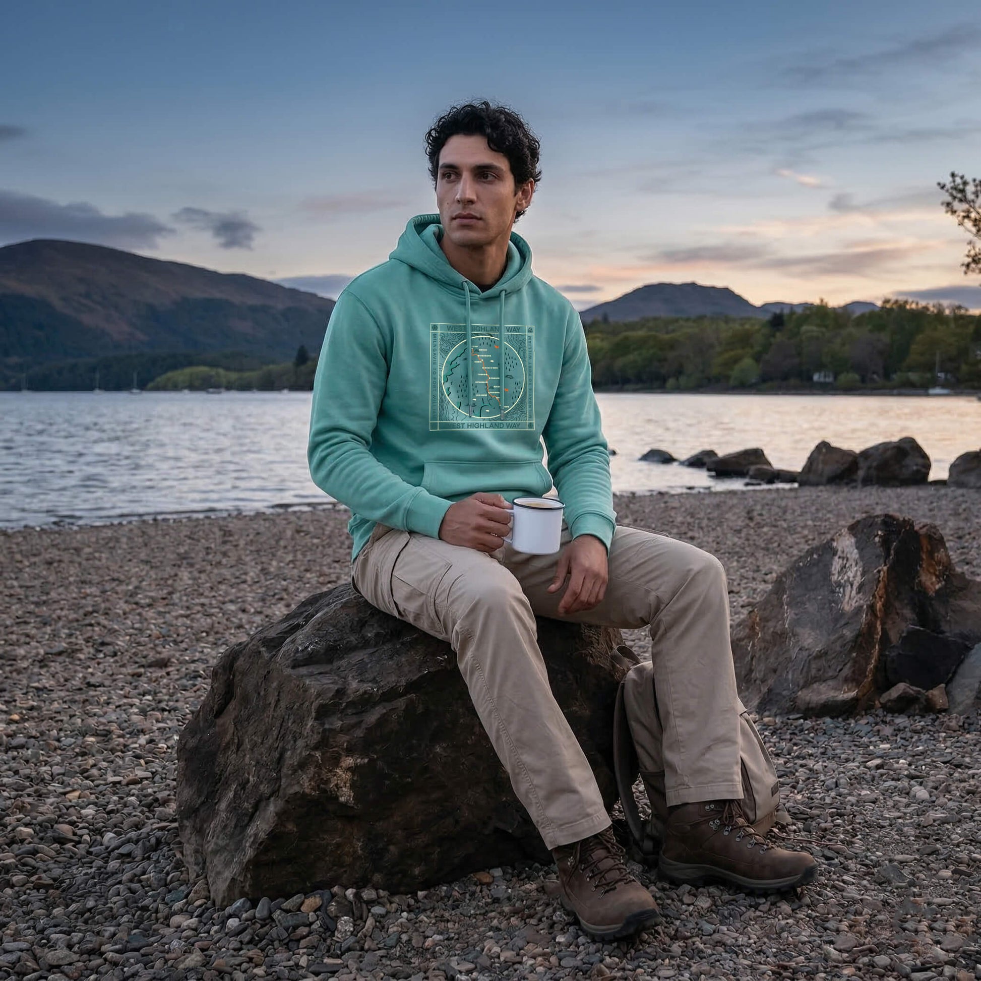 Three quarter view of seated man wearing teal west highland way map organic cotton hoodie